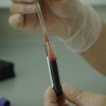 Foto de unas manos con guantes en el laboratorio sosteniendo un vial xcon sangre para toma de muestras
